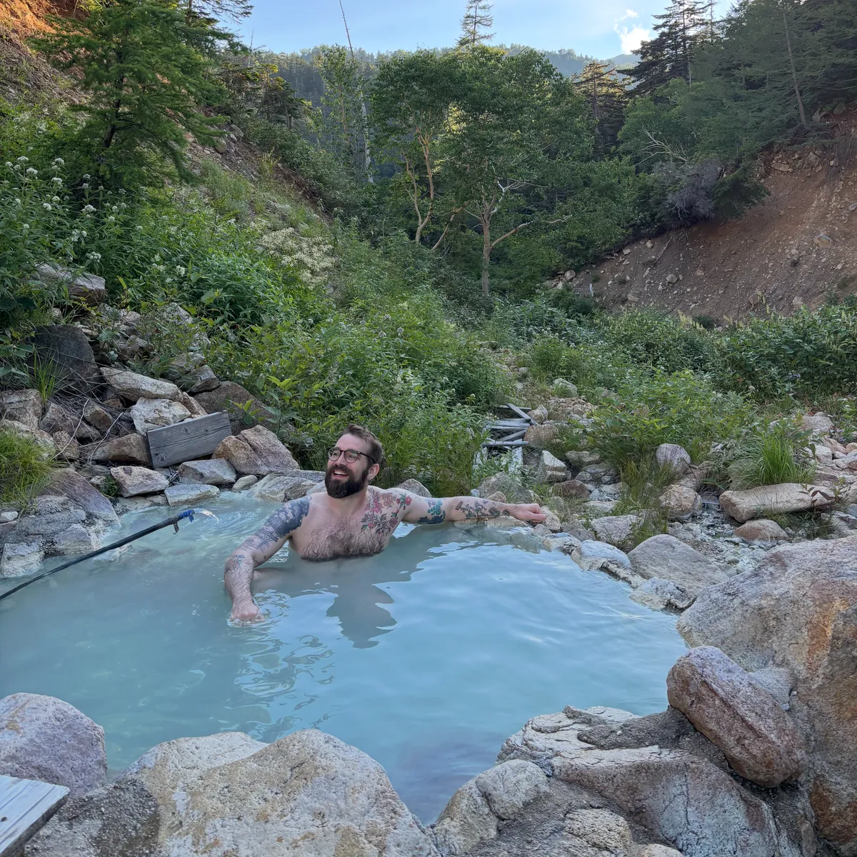 Josh soaking in an outdoor hot spring surrounded by forest